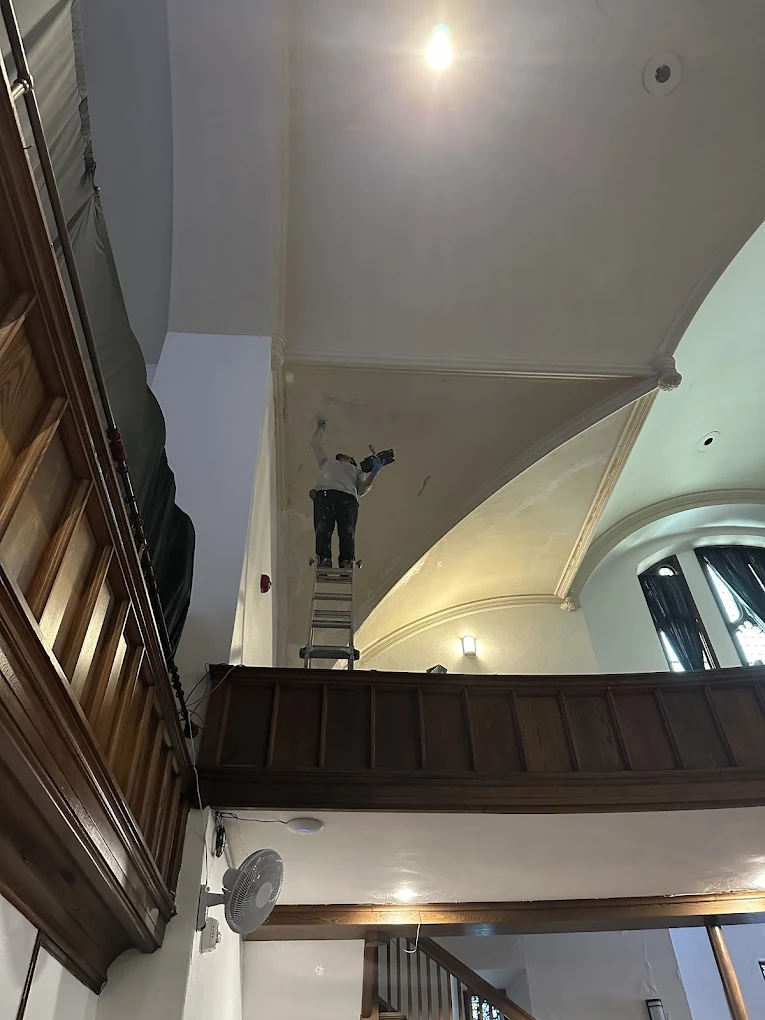 Painter restoring a tall arched ceiling inside a church