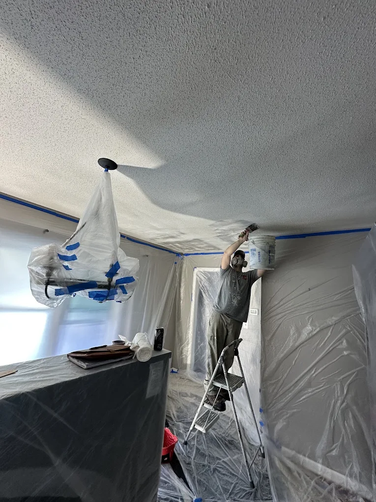 Painter applying material to a textured ceiling in a protected room