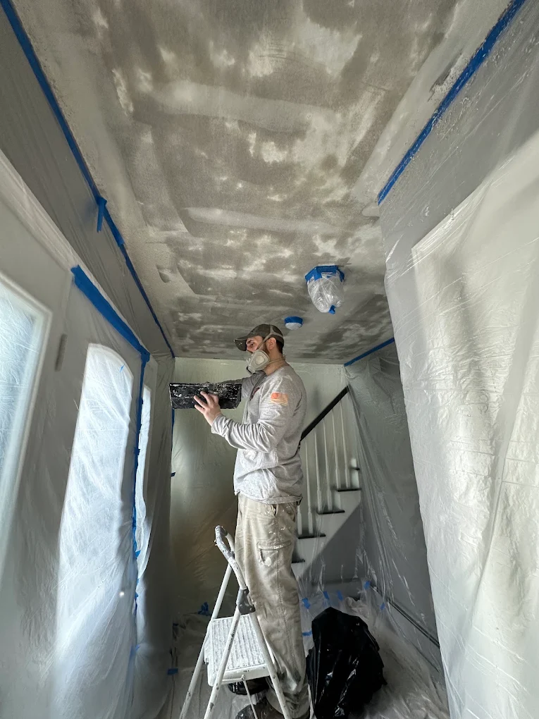 Painter repairing a textured ceiling in a fully masked hallway