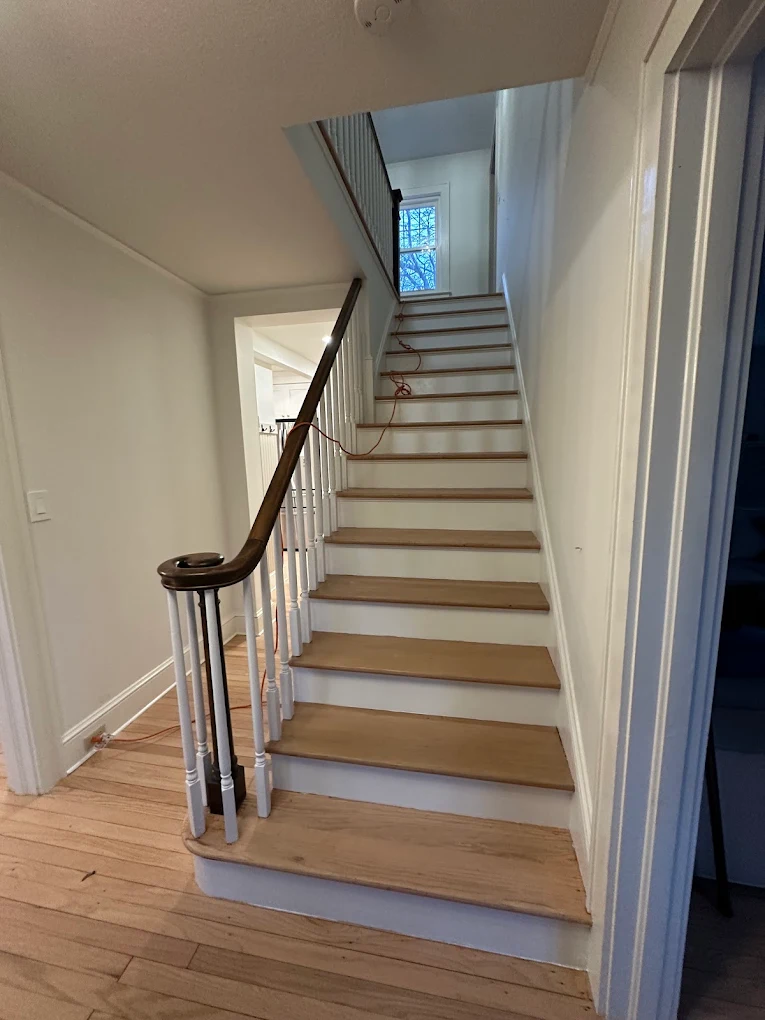 Staircase with white risers and balusters and a dark handrail