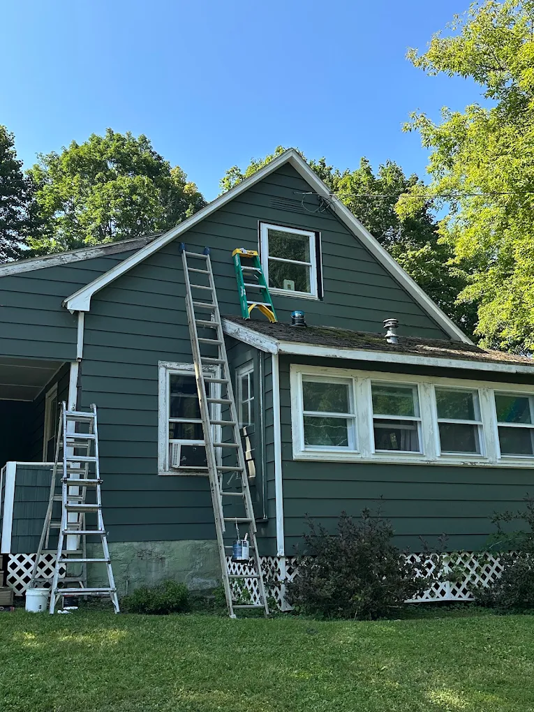 Ladders staged for a full exterior repaint of a green home