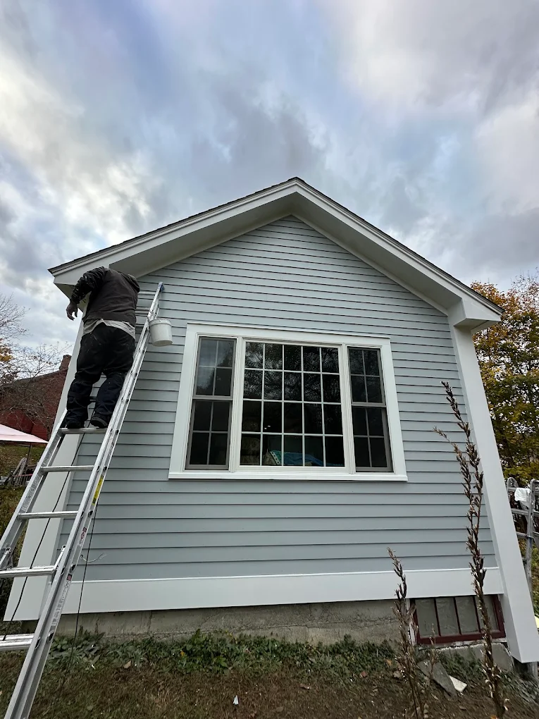 Painter on a ladder working on light blue siding and white trim