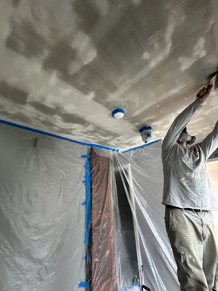 Painter skimming a ceiling with walls masked in plastic